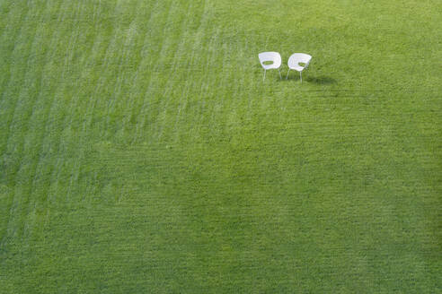 Zwei weiße Bürostühle auf grünem Rasen mit gemähtem Streifenmuster treffen sich in einer Ecke. - MINF16495