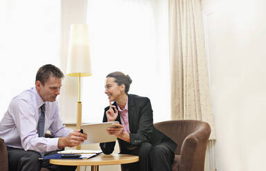 Businesswoman and man having meeting in hotel lobby or room, looking at ipad. - MINF16497