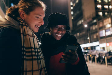 Italien, Lächelndes Paar mit Blick auf das Smartphone in der Stadt bei Nacht - ISF25522