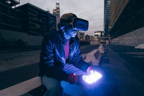 Italy, Woman usingVR goggles in city at dusk - ISF25530
