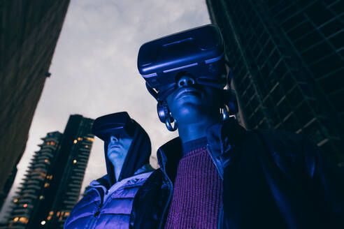 Italy, Couple withVRgoggles standing in city at dusk - ISF25534