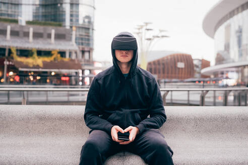 Italien, Mann mit VR-Brille sitzt auf Mauer in Stadt - ISF25540