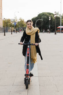 Glücklicher Teenager auf einem elektrischen Roller auf dem Fußweg - JRVF02363