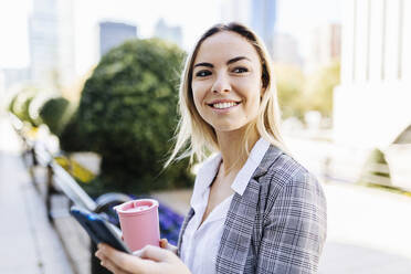 Happy businesswoman with reusable coffee cup and smart phone - XLGF02471