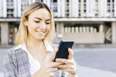 Lächelnde junge blonde Geschäftsfrau mit Smartphone - XLGF02477