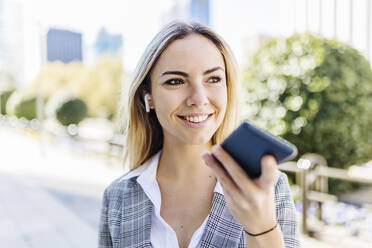 Glückliche junge Geschäftsfrau, die über den Lautsprecher ihres Smartphones spricht - XLGF02481