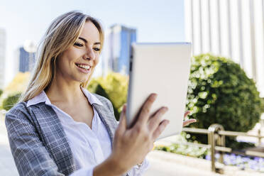 Lächelnde blonde Geschäftsfrau bei einem Videoanruf über einen Tablet-PC - XLGF02482