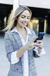 Smiling businesswoman with blond hair using smart phone - XLGF02496