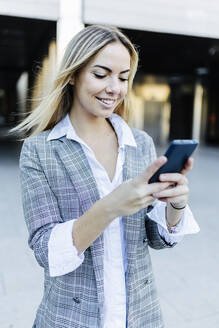 Lächelnde Geschäftsfrau mit blondem Haar, die ein Smartphone benutzt - XLGF02496