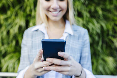 Lächelnde Geschäftsfrau, die eine Textnachricht über ihr Smartphone verschickt - XLGF02502