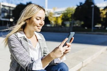 Lächelnde blonde berufstätige Frau mit Smartphone an einem sonnigen Tag - XLGF02507