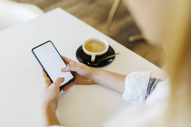 Businesswoman using smart phone by coffee cup in cafe - XLGF02519