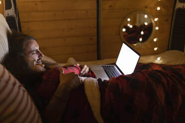 Pärchen mit Laptop auf dem Bett im Wohnmobil liegend - EGHF00305
