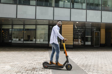 Junger Mann fährt mit einem elektrischen Roller auf dem Gehweg - VYF00859