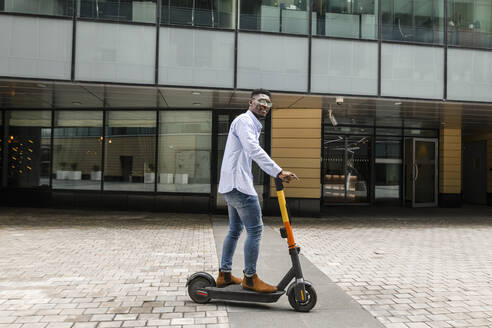 Young man riding electric push scooter on footpath - VYF00859