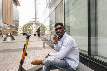 Thoughtful man talking on smart phone in front of building - VYF00869