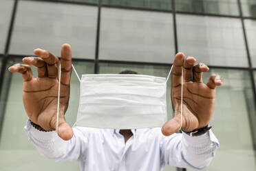 Man showing surgical mask in front of glass wall - VYF00872