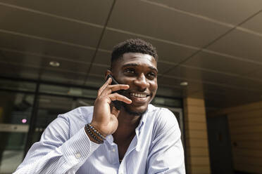 Lächelnder junger Mann, der mit einem Mobiltelefon spricht - VYF00899