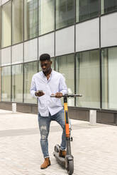 Young man with push scooter using mobile phone on footpath - VYF00901