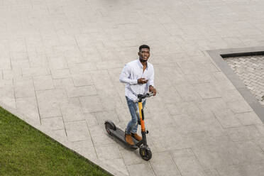 Young man with electric push scooter on footpath - VYF00913