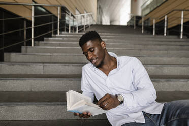 Lächelnder Mann, der auf einer Treppe ein Buch liest - VYF00917