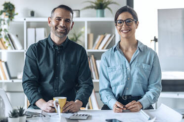 Smiling businessman and businesswoman at desk in small office - JSRF01765