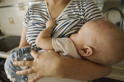 Mother's carrying toddler and breastfeeding at home - EYAF01868