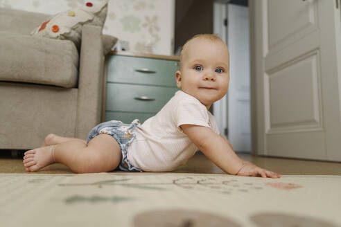 Smiling baby girl lying on floor at home - EYAF01869