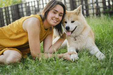 Lächelnde Frau mit Akita-Hund im Gras - SEAF00321