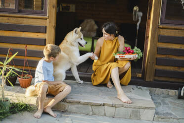 Frau hält Gemüsetablett in der Hand und schüttelt den Hund, der neben ihrem Sohn an der Tür sitzt - SEAF00322