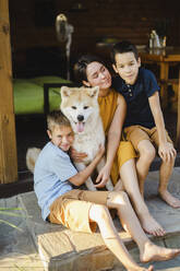 Mother and sons sitting at doorway with Akita dog - SEAF00323