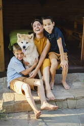 Smiling mother sitting with sons and Akita dog at doorway - SEAF00326