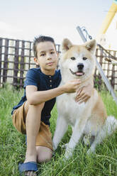 Cute boy with Akita dog sitting on grass - SEAF00330