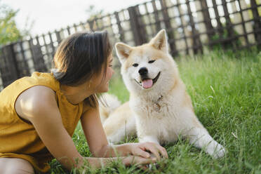 Verspielte Frau sieht Akita-Hund im Gras sitzend an - SEAF00336