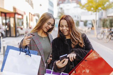Glückliche Frauen mit Einkaufstüten, die auf ihr Smartphone schauen - DAWF02382