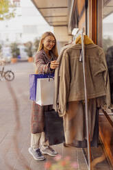 Smiling woman buying clothes hanging for sale outside store - DAWF02387