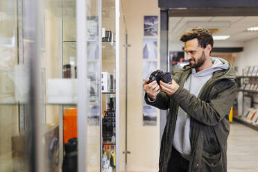 Smiling man examining camera in retail store - DAWF02395