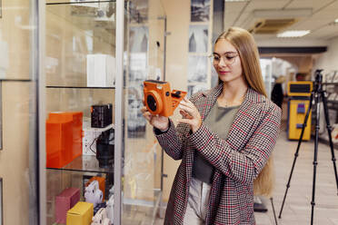 Junge Frau prüft Sofortbildkamera in Geschäft - DAWF02399