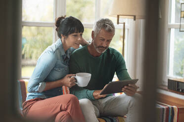 Mann mit Tablet-PC neben Frau mit Kaffeetasse zu Hause sitzend - JOSEF06369