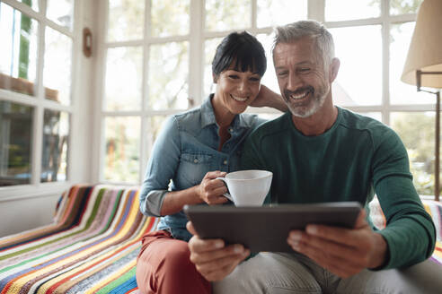 Lächelnder Mann, der einen Tablet-PC mit einer Frau teilt, die eine Kaffeetasse zu Hause hält - JOSEF06378