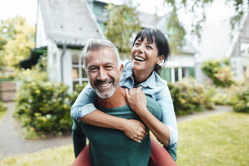 Happy man giving piggyback ride to woman in backyard - JOSEF06390