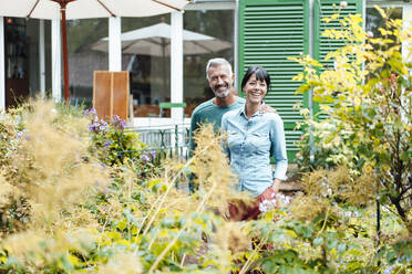 Happy man arm around woman amidst plants in backyard - JOSEF06393