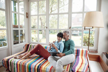 Man sharing tablet PC with woman holding coffee cup on sofa - JOSEF06411