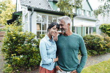 Smiling mature man looking at woman standing with hand on shoulder in backyard - JOSEF06434