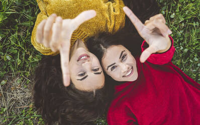 Happy sisters lying on grass making finger frame - JCCMF05006