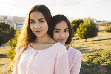 Smiling woman behind twin sister in park - JCCMF05011