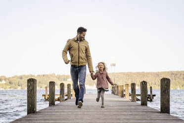 Cheerful man and girl running together on jetty - DIGF17373