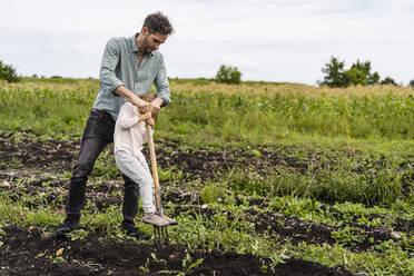 Tochter steht auf einer vom Vater geschobenen Mistgabel auf einem Feld - DIGF17400