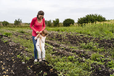 Mother teaching daughter to harvest potatoes in field - DIGF17404