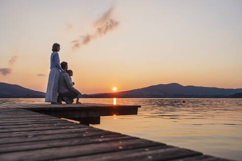 Family with daughter looking at sunset view from jetty, Mondsee, Austria - DIGF17409